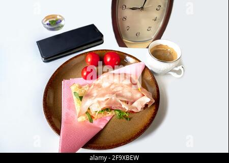 Sandwich avec salami et rucola, tomate cerise sur l'assiette, tasse d'espresso, montre, mobile et fleurs sur fond blanc, petit déjeuner. Banque D'Images