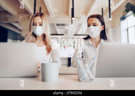 Deux collègues femmes travaillant ensemble au bureau portant des masques médicaux Banque D'Images