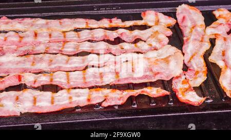 Cuisson de tranches de bacon sur un barbecue à gaz extérieur. Banque D'Images