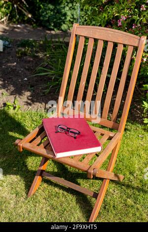 Un grand livre de couverture rigide reposant sur une chaise avec une paire de lunettes de lecture placées sur le dessus. Lecture en extérieur concept Banque D'Images