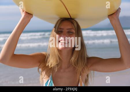 Femme caucasienne souriante portant un bikini portant une planche de surf jaune sur elle rendez-vous à la plage Banque D'Images