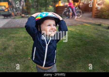 Mignon petit adorable caucasien joyeux tout-petit garçon mis sur la tête casque de sécurité va avoir le plaisir de l'équitation scooter de kick, voyage à vélo dans le siège d'enfant de vélo Banque D'Images