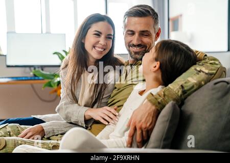 Joyeux homme militaire masculin qui embrasse sa famille tout en étant assis dessus canapé à l'intérieur Banque D'Images