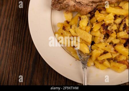 Pommes de terre frites maison et un grand morceau de viande sur une assiette blanche. Gros plan. Banque D'Images