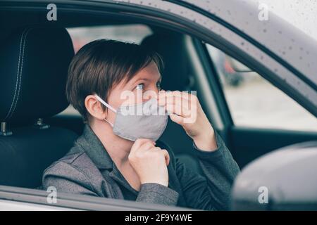 Femme portant un masque de protection en voiture pendant les pandémies de Covid-19, regardant le miroir, foyer sélectif Banque D'Images