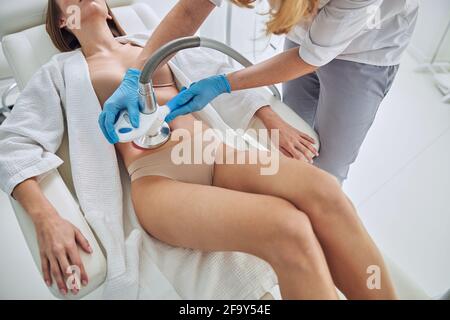 Femme non reconnue en peignoir blanc recevant le contour du corps par cavitation à ultrasons traitement en clinique de bien-être Banque D'Images