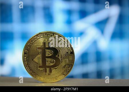 Une version physique de Bitcoin BTC avec un arrière-plan bleu flou et une flèche. Banque D'Images