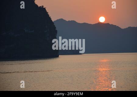 Vue panoramique du coucher de soleil sur les eaux étincelantes, les formations rocheuses, les montagnes bleues et les bateaux flottants sur la baie de Halong au Vietnam Banque D'Images