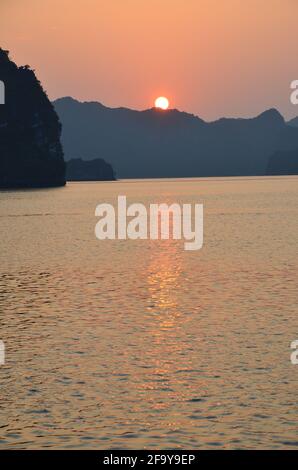 Vue panoramique du coucher de soleil sur les eaux étincelantes, les formations rocheuses, les montagnes bleues et les bateaux flottants sur la baie de Halong au Vietnam Banque D'Images