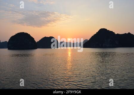 Vue panoramique du coucher de soleil sur les eaux étincelantes, les formations rocheuses, les montagnes bleues et les bateaux flottants sur la baie de Halong au Vietnam Banque D'Images