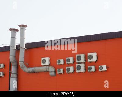 Un fragment de bâtiment orange avec de nombreux climatiseurs suspendus sur le mur et deux tuyaux de ventilation Banque D'Images