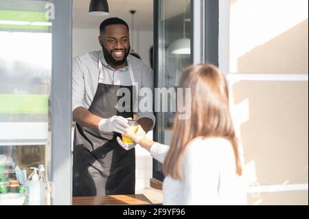 Un serveur afro-américain souriant et souriant sert une cliente féminine, un gérant de café multiracial tient une commande à emporter par une fenêtre à emporter Banque D'Images