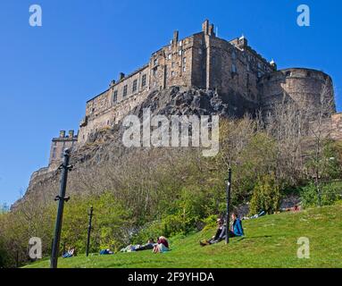 Édimbourg, Écosse, Royaume-Uni. 21 avril 2021. Les gens assis au soleil au-dessus du Grassmarket et au-dessous du château d'Édimbourg, température 10 degrés centigrade avec un vent froid. Banque D'Images