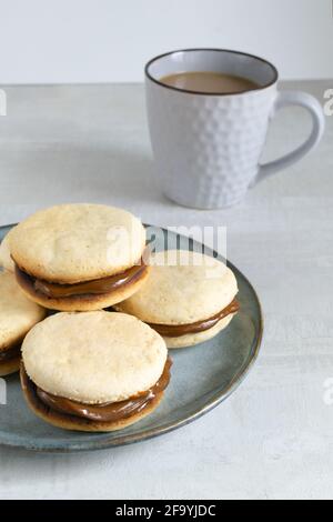Biscuits Alfahores au lait condensé sur une assiette grise avec une tasse de café. Biscuits maison traditionnels. Concept de cuisine maison. Orientation verticale Banque D'Images