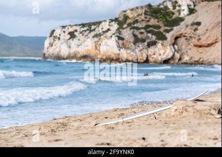 Gros plan d'une planche de surf sur une plage de sable avec des surfeurs flous en arrière-plan. Banque D'Images