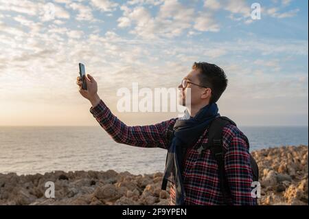 Jeune homme dans un endroit isolé sur une falaise rocheuse avec la mer sur fond. Homme tenant le smartphone pour tenter de capter le signal. Banque D'Images