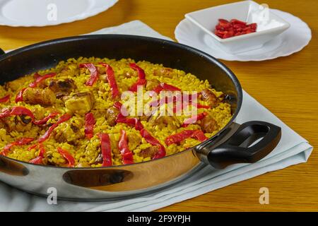 Paella traditionnelle espagnole de fruits de mer avec saucisses de porc, côtes de porc et poivrons rouges dans une poêle décorée d'une assiette de poivre rouge et d'une cuillère. Banque D'Images