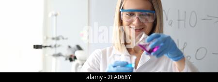 Femme scientifique dans des lunettes de sécurité en versant une solution chimique dans un flacon en laboratoire Banque D'Images