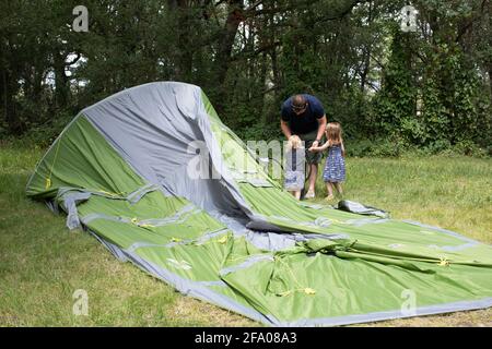 Un père mettant une grande tente avec l'aide de ses filles en vacances dans un camping. Banque D'Images