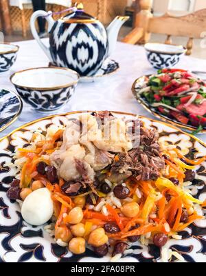 Une table dans un restaurant ouzbek: Pilaf de mariage fait de riz avec des carottes. Avec agneau et poulet. Ainsi que des raisins secs, des pois chiches et des œufs. Sur flou Banque D'Images