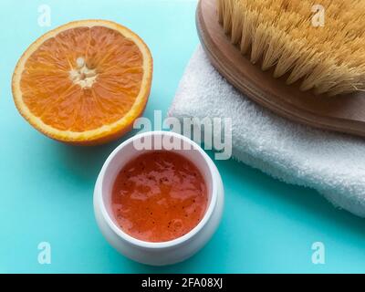 Un pot de gommage à l'orange, une brosse pour le corps sur une serviette blanche pliée et un demi-fruit orange sur fond bleu. Concept spa, nettoyage et hydratation du corps, Banque D'Images