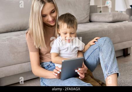 Une jeune maman assise à la maison avec un enfant regardant des films sur une tablette. Banque D'Images