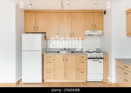 Une cuisine en érable dans un appartement vide de la ville avec des appareils électroménagers blancs, des comptoirs en granit, beaucoup d'armoires pour le stockage, et des planchers de bois franc. Banque D'Images