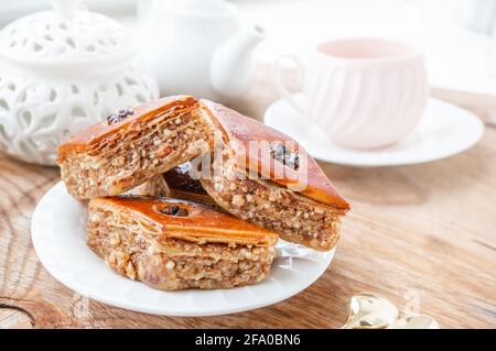 Trois morceaux de baklava aux noix sur une assiette blanche, une cuillère à café, une belle tasse de thé, une théière sur une table en bois. Copier l'espace. Banque D'Images