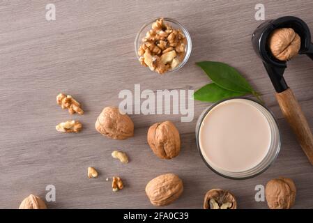 Verre rempli de lait de légumes de noix avec fruits et table en bois avec casse-noisette. Vue de dessus. Banque D'Images