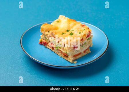 Gros plan avec une portion de lasagnes végétariennes sur une assiette bleue. Tranche de lasagne maison sur une table bleue. Banque D'Images