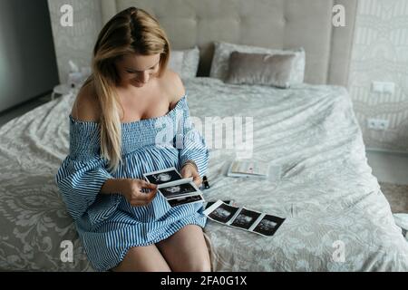 Une femme enceinte heureuse regardant des images échographiques de son bébé. Un portrait d'une jeune femme enceinte souriante qui passe par des photos numérisées. Banque D'Images