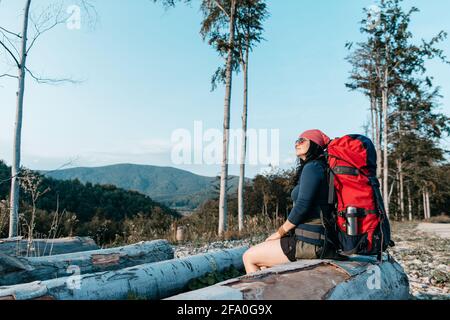 Une randonneur se reposant et profitant du coucher du soleil. Un portrait d'une femme avec un sac à dos prenant une pause et en admirant la vue. Banque D'Images