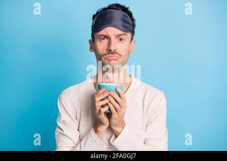 Photo portrait d'un homme fatigué contrarié tenant une tasse de thé dedans deux mains isolées sur un arrière-plan bleu vif Banque D'Images