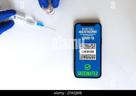 Smartphone avec passeport vaccinal sur la table du médecin, mains dans des gants avec seringue et flacon de vaccin COVID-19, fond blanc, concept de voyage sûr p Banque D'Images