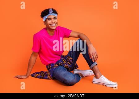 Photo de la taille du corps pleine longueur d'un jeune homme heureux assis porter un t-shirt rose jean toile chaussures isolées couleur orange vif arrière-plan Banque D'Images