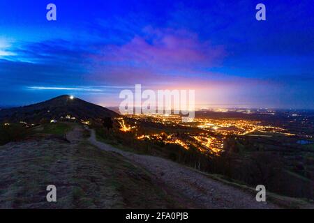 Great Malvern, Worcestershire, Royaume-Uni. 21 avril 2021. Les lumières de Great Malvern, et au loin, la ville de Worcester, illuminent les nuages avec Worcestershire Beacon sur les collines Malvern silhoueted. Les deux prochains jours promettent d'être ensoleillés et chauds dans tout le Royaume-Uni. Crédit : Peter Lophan/Alay Live News Banque D'Images