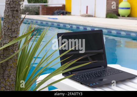 Ordinateur portable sur une chaise longue au bord de la piscine. Banque D'Images