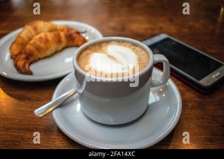 Latte café avec croissants gras et téléphone portable. Banque D'Images