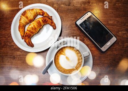 Latte café avec croissants gras et téléphone portable. Banque D'Images