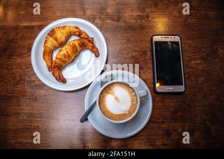 Latte café avec croissants gras et téléphone portable. Banque D'Images