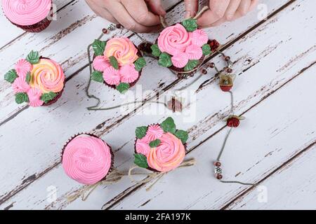 Cupcakes en velours rouge, ornés de dentelle de sisal, entourés d'un collier féminin. Confiseur décorant un cupcake (vue de dessus). Banque D'Images