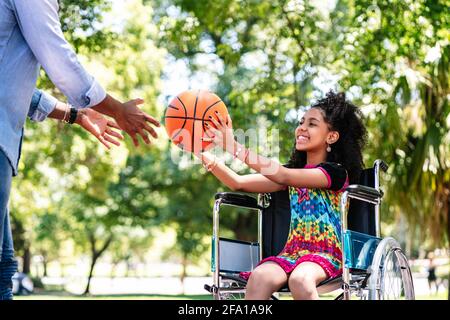 Petite fille en fauteuil roulant jouant au basket-ball avec son père. Banque D'Images