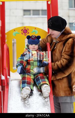 La mère tient son tout-petit sur un toboggan en hiver Banque D'Images