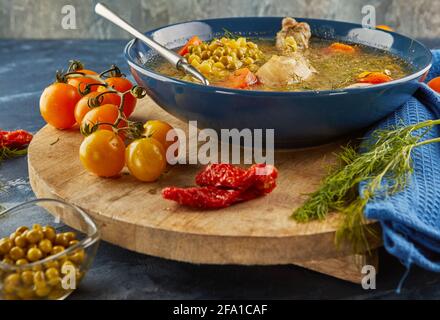 Soupe aux pois avec poulet, carottes, tomates et herbes dans une assiette profonde sur bois avec serviette sur fond bleu. Banque D'Images