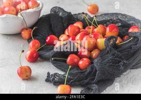Cerises douces orange mûres de type « Anne royale » sur un tissu noir, bol blanc avec cerises en arrière-plan Banque D'Images
