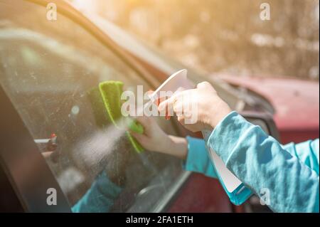 Femme nettoyage des vitres de voiture avec du spray nettoyant. Femme nettoyage des mains des vitres de voiture avec un chiffon en microfibre. Main avec le spray nettoyant vitre d'essuyage d'une voiture o Banque D'Images