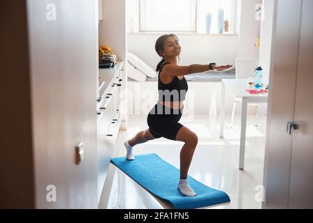 Jeune femme gaie pratiquant le yoga à la maison Banque D'Images