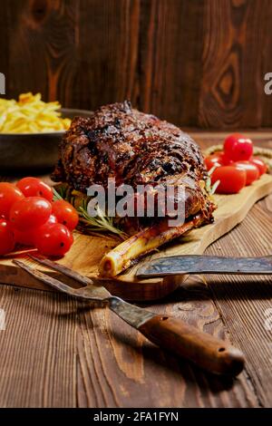 Cuisse d'agneau entière cuite sur une planche à découper en bois avec garniture Banque D'Images