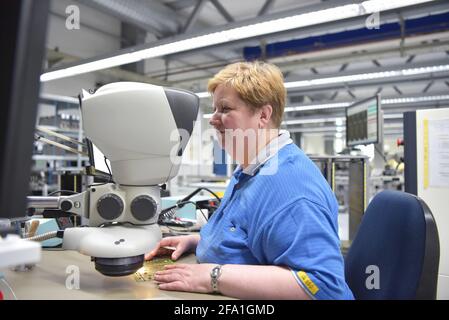 Femme dans une usine pour la production de composants électroniques vérifie la qualité d'un conseil assemblé avec l'aide d'un microscope ou une loupe gl Banque D'Images