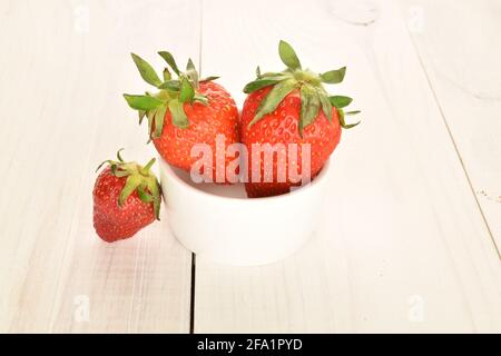 Trois fraises douces, avec des plats en céramique blanche sur une table en bois peinte. Banque D'Images